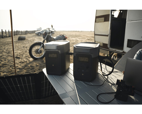 Szene mit zwei Stromgeneratoren auf einem Tisch im Freien mit einem Motorrad, einem Auto und einem Wohnwagen im Hintergrund.