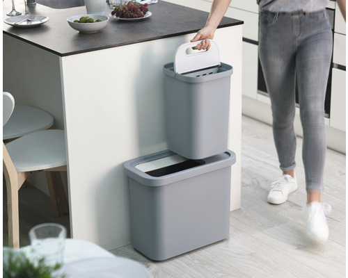 Collecteur de matières recyclables gris en deux parties dans la cuisine, avec une femme tenant le récipient supérieur.