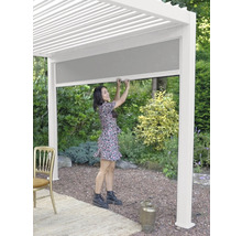 Une femme manipule un store latéral sous un toit de terrasse dans le jardin.