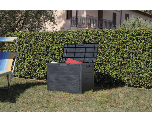 Geöffnete Gartenbox aus Kunststoff auf einer Rasenfläche vor einer Hecke.