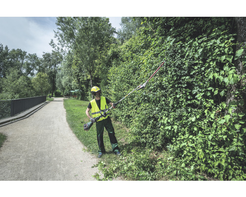 Une personne coupe une haie dans un parc avec un taille-haie sans fil.