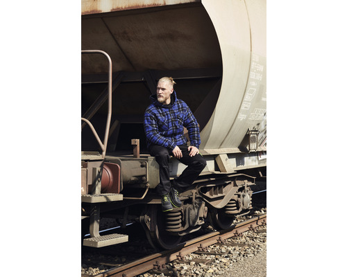 Mann mit karierter Jacke und Arbeitsschuhen sitzt auf einem Güterwagen