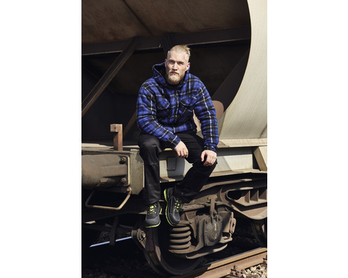 Mann mit karierter Jacke, Hose und Arbeitsschuhen sitzt auf einem Güterwagen
