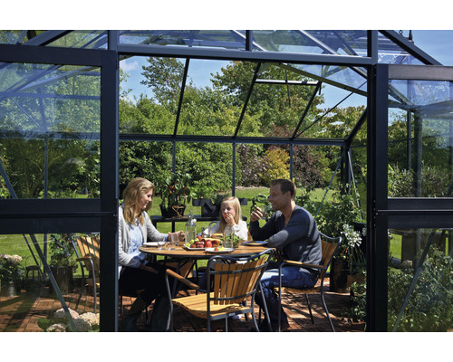 Une famille est assise à une table dans une serre aux parois en verre.