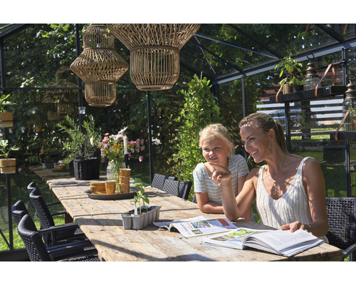 Intérieur de serre avec table en bois, chaises, plantes et deux personnes