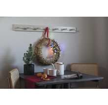 Intérieur décoratif avec couronne de paille, guirlande lumineuse, portemanteau, table, chaise et service à thé.