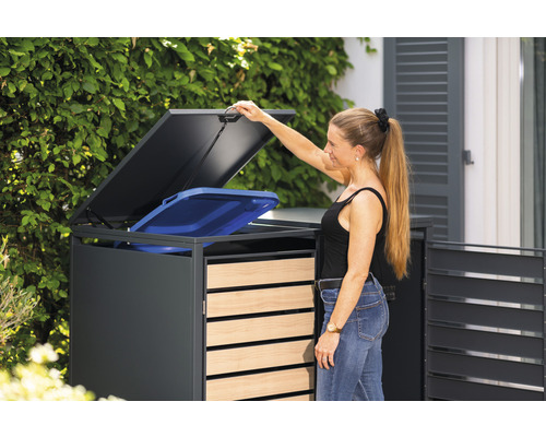 Frau öffnet Mülltonnenbox mit einem blauen Müllbehälter