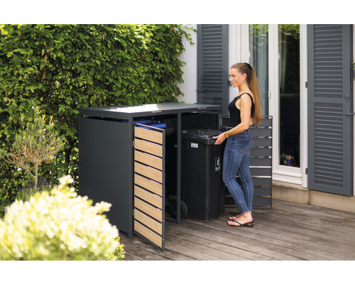 Mülltonnenbox im Garten mit Frau beim Einsetzen einer Mülltonne