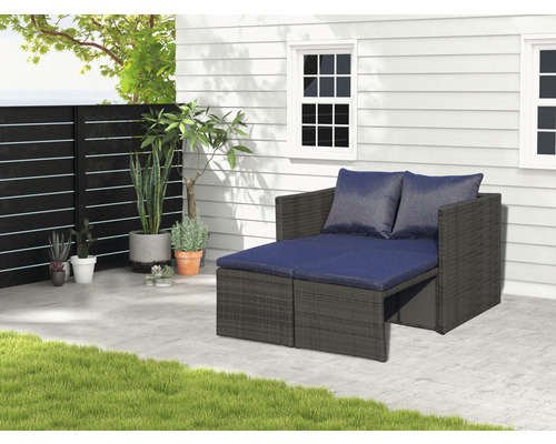 Gartenszene mit einem modularen Loungesofa mit dunkelgrauem Rattanrahmen und blauen Kissen auf einer Terrasse.