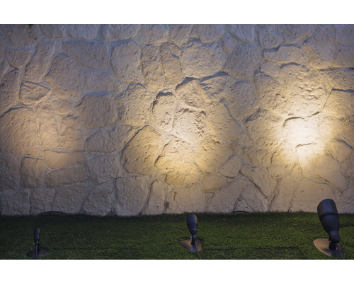 Mur de pierre éclairé par des spots de jardin sur une pelouse
