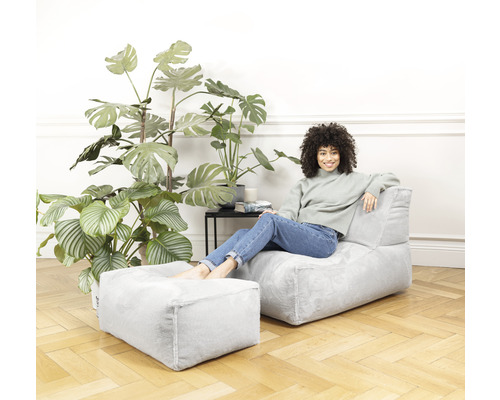 Femme se détend sur un fauteuil avec repose-pieds dans le salon avec des plantes