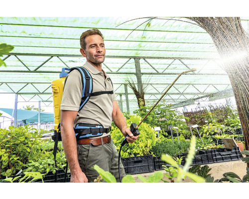 Un homme utilise un pulvérisateur à dos pour l''entretien des plantes dans une serre.