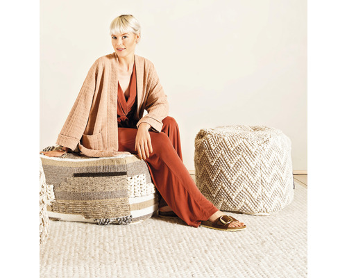 Frau sitzt auf einem quadratischen Pouf aus verschiedenen Materialien in einem hellen Raum.