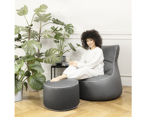 Une femme est assise sur un pouf gris avec un repose-pieds dans le salon.