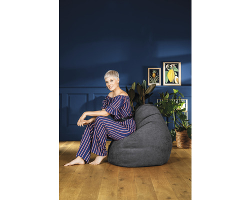 Femme assise sur un pouf gris dans une pièce à vivre avec des plantes et de la décoration