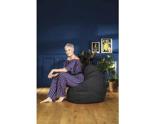 Frau sitzt auf einem schwarzen Sitzsack in einem Raum mit Pflanzen und Dekoration