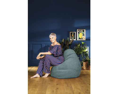 Frau sitzt auf einem Sitzsack in einem Wohnzimmer mit Pflanzen und Bildern an der Wand