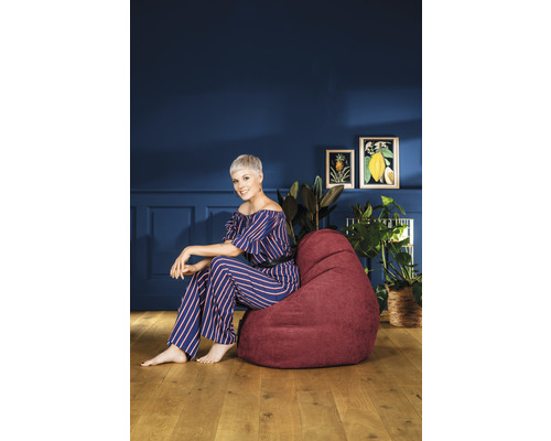 Frau sitzt auf einem roten Sitzsack in einem Wohnzimmer mit Pflanzen und Bildern an der Wand