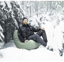 Un homme est assis sur un pouf dans la neige dans un paysage forestier enneigé.