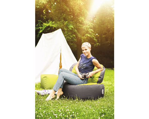 Scène avec une femme assise sur un pouf d''extérieur devant une tente