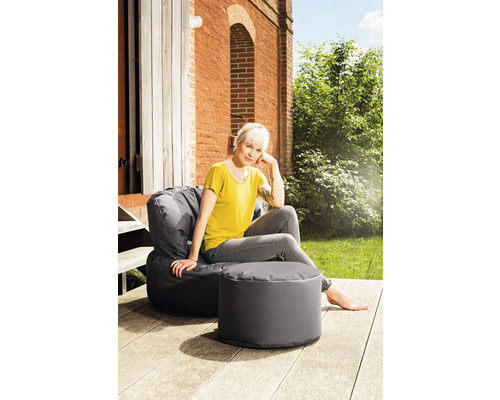 Une femme est assise et se détend dans un fauteuil poire gris avec un repose-pieds à l''extérieur.