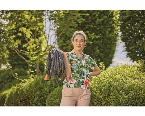 Frau hält einen Gartenschlauch im Garten.