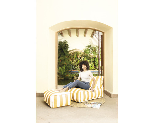 Frau sitzt in einem Raum auf einem gestreiften Sitzsack mit Fußhocker
