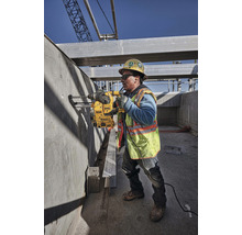 Un ouvrier du bâtiment perce un trou dans un mur en béton avec une perceuse sur un chantier.