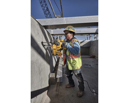 Un ouvrier du bâtiment perce un trou dans un mur en béton avec une perceuse sur un chantier.