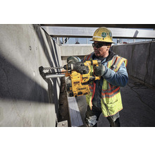 Un ouvrier du bâtiment perce un mur en béton avec une perceuse DeWalt sur un chantier.