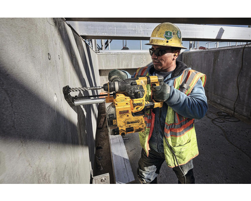 Un ouvrier du bâtiment perce un mur en béton avec une perceuse DeWalt sur un chantier.