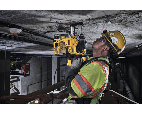 Un ouvrier perce un trou dans un plafond en béton avec une carotteuse DeWalt.
