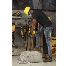 Un ouvrier portant un casque de sécurité utilise un marteau perforateur pour travailler un morceau de béton.