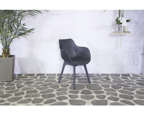 Chaise de jardin noire en plastique sur un sol en pierre devant un mur