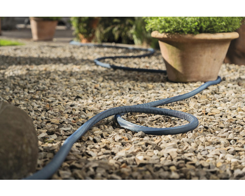 Tuyau d''arrosage bleu posé sur un chemin de gravier à côté de pots de fleurs.