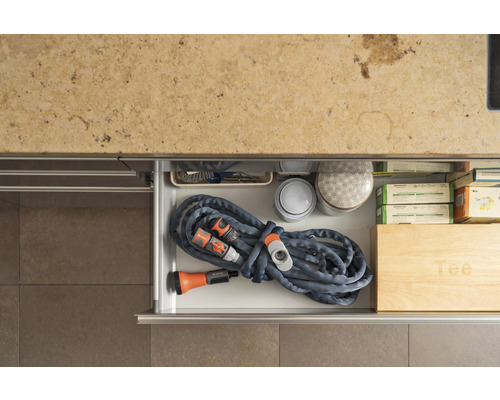 Gartenschlauch mit Spritze und Kupplungen in einer Schublade zusammen mit anderen Gartengeräten.