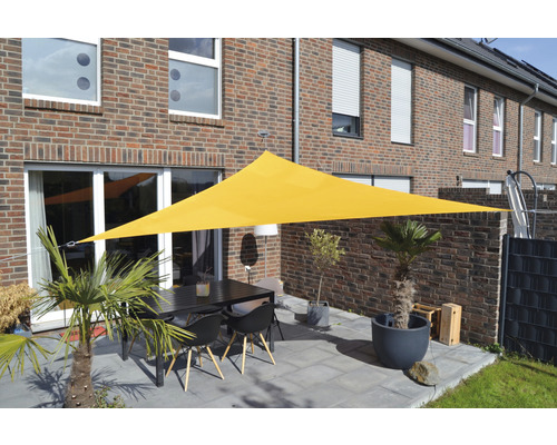 Gelbes dreieckiges Sonnensegel über einer Terrasse mit Tisch und Stühlen vor einem Wohnhaus.