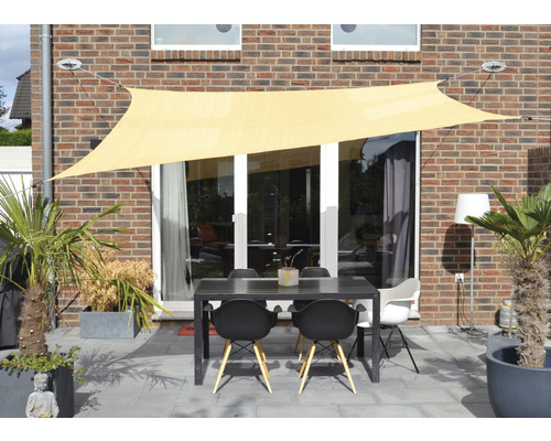Espace extérieur avec voile d''ombrage, table et chaises sur une terrasse devant une maison.