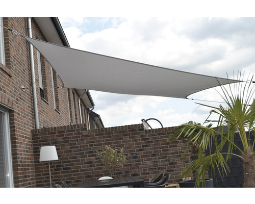 Dreieckiges Sonnensegel über einer Terrasse mit Ziegelmauer und Gartenmöbeln