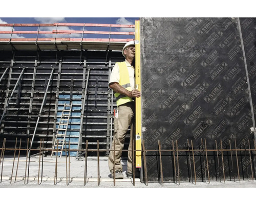 Ein Bauarbeiter mit Helm und Warnweste nivelliert die Betonschalung mit einer Wasserwaage.