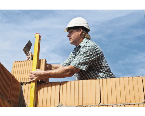 Maurer mit Wasserwaage und Kelle beim Bau einer Ziegelwand