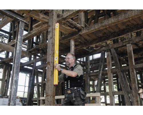 Handwerker mit Wasserwaage an Holzbalken im Rohbau