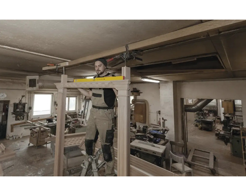 Ein Handwerker arbeitet mit einer Wasserwaage an einem Holzrahmen in einer Werkstatt.