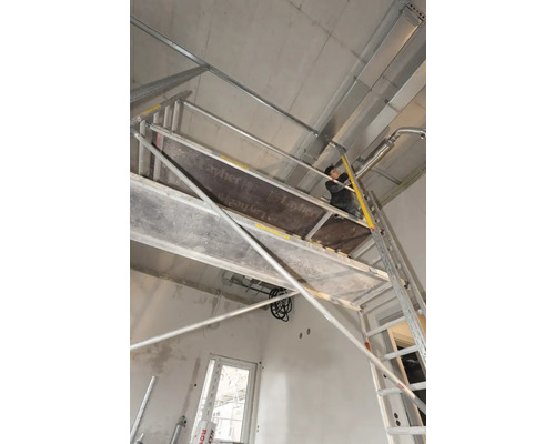 Un ouvrier sur un échafaudage effectuant des travaux de plafond dans un intérieur.