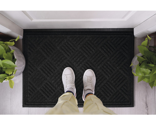 Paillasson noir avec motif géométrique devant une porte