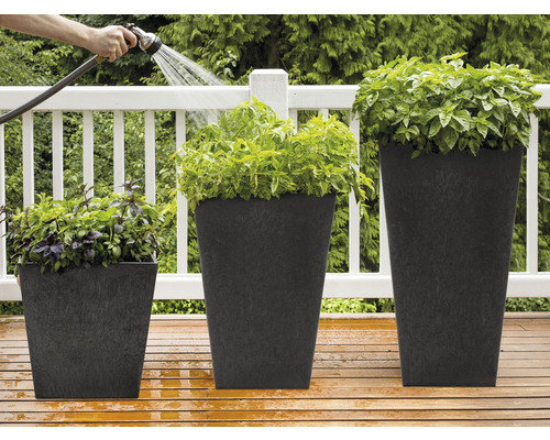 Drei bepflanzte, quadratische Pflanzgefäße unterschiedlicher Größe werden mit einem Gartenschlauch bewässert.