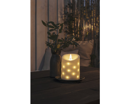 Bougie LED décorative à motifs à points sur une table, à côté d''un vase avec des branches.