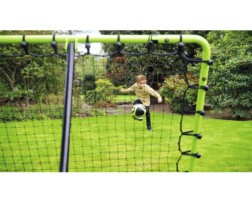Un garçon joue avec un ballon devant un but de football dans le jardin.