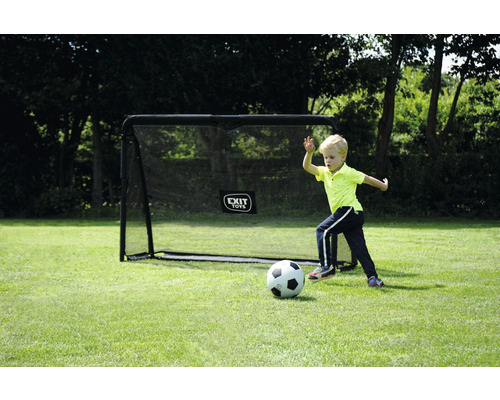 Junge spielt Fußball vor einem Fußballtor im Garten.