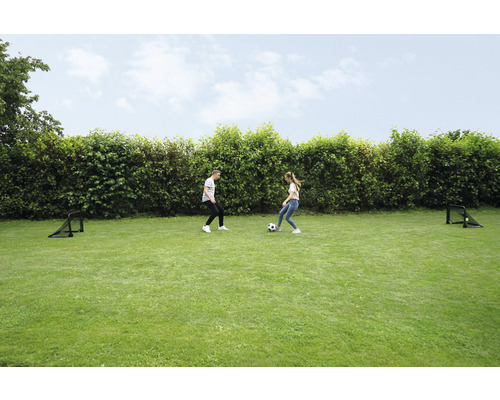Zwei Personen spielen mit einem Fußball auf einer Rasenfläche mit zwei Fußballtoren.